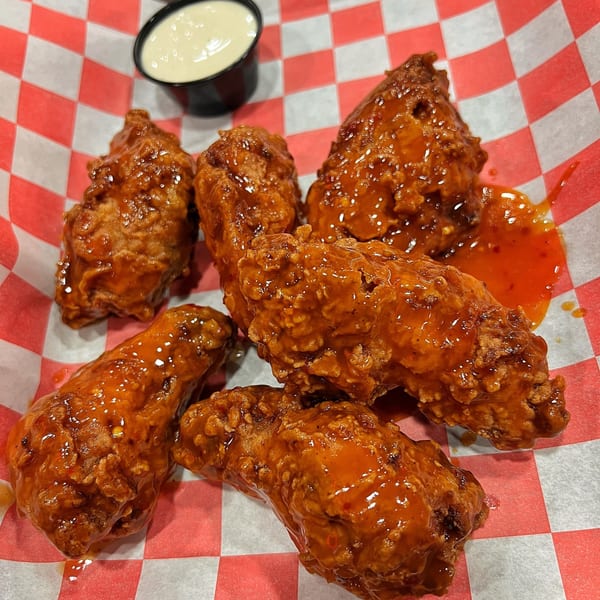 Six hot chicken wings with sauce and a side of ranch dressing on red and white checkered paper.