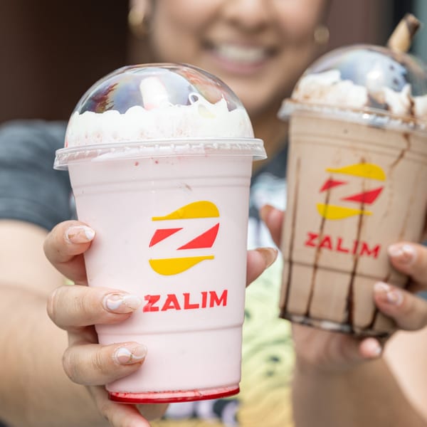 A person holding two Zalim Hot Chicken & Burgers milkshakes, one strawberry and one chocolate.