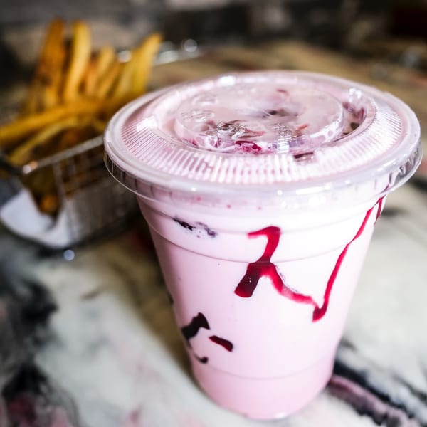 Pink milkshake with berry drizzle and a side of fries on a marble table at Zalim Hot Chicken & Burgers.
