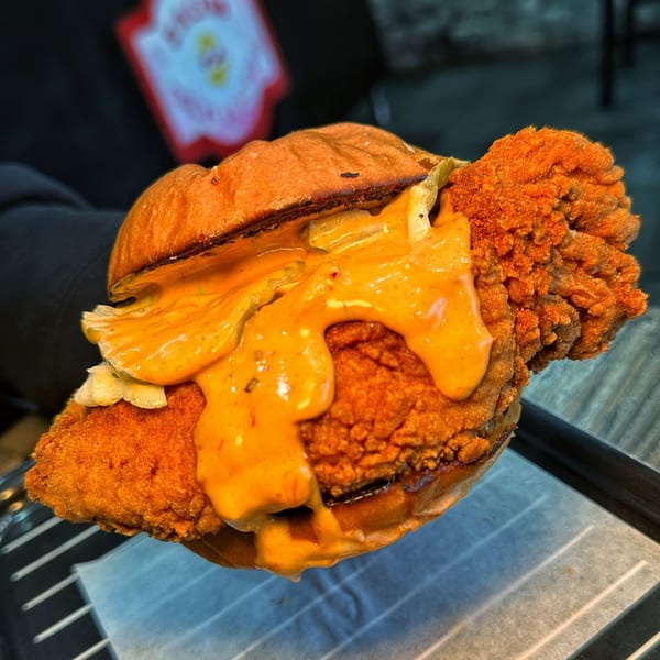 A close-up of a Zalim Hot Chicken & Burgers sandwich with crispy chicken and orange sauce.