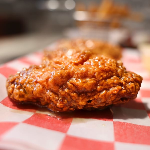 Close-up of a crispy, glazed hot chicken wing on red and white checkered paper.