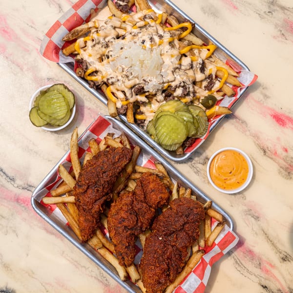 Two trays of Zalim Hot Chicken & Burgers food: loaded fries with cheese and meat, and spicy chicken tenders with fries.
