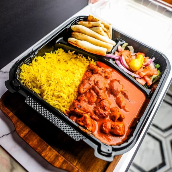 Chicken tikka masala with yellow rice, naan bread, and a side salad in a takeout container.